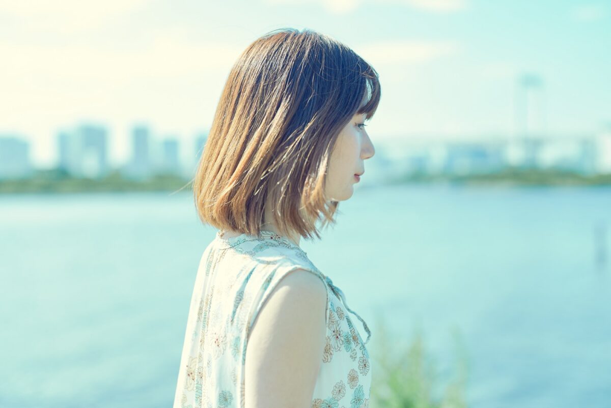 水辺を背景に伏し目で横顔を見せる女性のポートレート